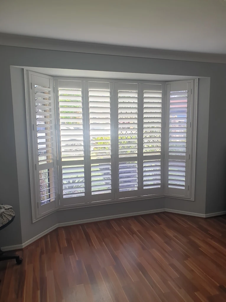 White plantation shutters in a bay window above timber flooring